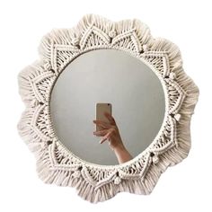 a hand holding a cell phone in front of a white circular mirror with fringes on it