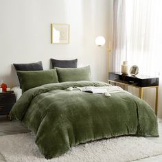 a bed with green comforter and pillows in a room next to a white rug