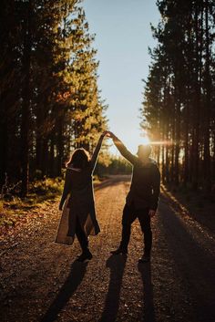 a man and woman holding hands while standing on a road in the middle of trees
