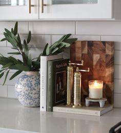 a candle and some books on a white counter top next to a potted plant