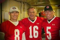 three men in red football uniforms posing for a photo together, with one man wearing a hat and the other smiling