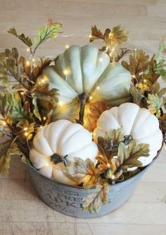 some white pumpkins are in a bucket with leaves and lights on the floor next to it