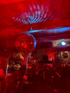 people are dancing at a party with disco balls in the foreground and red lights on the ceiling