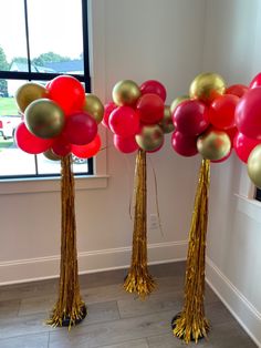 three tall gold and red balloons in front of a window