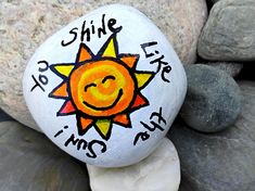 a painted rock with the words smile and a sun on it, sitting next to some rocks