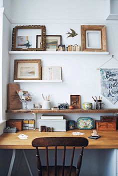 a wooden desk topped with lots of pictures and other items next to a wall mounted shelf