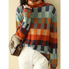 a woman wearing a multicolored sweater and white pants holding a handbag in front of her face