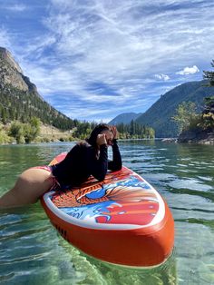 a woman laying on top of a surfboard in the water with mountains in the background