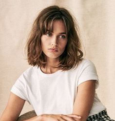 a woman sitting on top of a chair wearing a white shirt and checkered pants