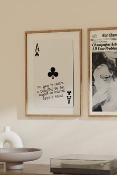 two framed pictures hang on the wall above a table with a bowl and vase next to it