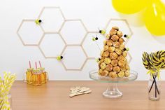 a table topped with desserts and balloons next to honeycomb wall art pieces on the wall