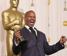 a man in a suit and tie holding an oscar for best supporting actor on stage