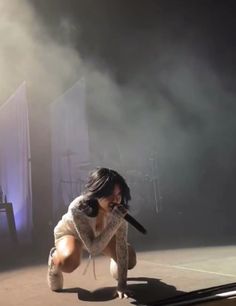 a woman kneeling down on top of a stage holding a microphone in front of her face