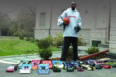 a man holding a basketball standing in front of a pile of toy cars on the ground
