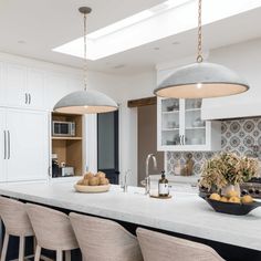 a kitchen with white cabinets and marble counter tops, two pendant lights over the island