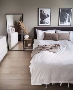 a white bed sitting in a bedroom next to two pictures on the wall and a dresser