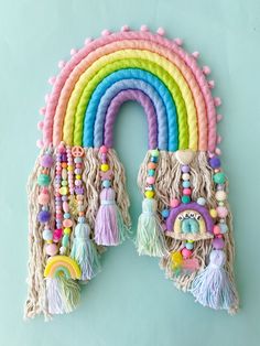 a rainbow shaped wall hanging with tassels and beads on the ends, in pastel colors