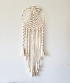 a white wall hanging with some tassels on it's sides and a wooden shelf below