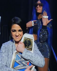 two women with blue hair and one is holding a wrestling belt in front of her