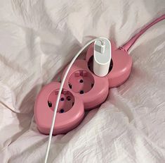 three pink electrical outlets are plugged into an outlet on a white sheeted bed