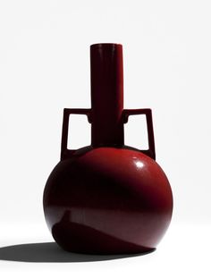 a red vase sitting on top of a white table next to a black object in the middle