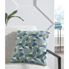 a blue and green pillow sitting on top of a white chair next to a potted plant