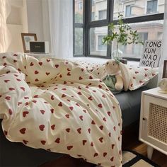 a bed with white sheets and red hearts on it in front of a large window