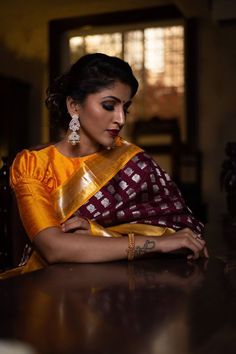 a woman sitting at a table wearing a yellow and maroon sari