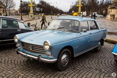 an old blue car is parked on the cobblestone street next to other cars