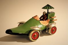 a green toy car with a man in the driver's seat and an umbrella on top
