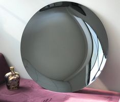 a round mirror sitting on top of a purple table next to a vase and bottle