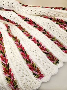 a white crocheted blanket with red, green and pink flowers on it sitting on top of a table