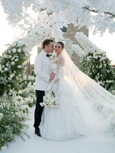 a bride and groom standing in front of an archway with white flowers on the side