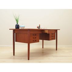 a wooden desk with two drawers and a vase on it's top, in front of a white wall