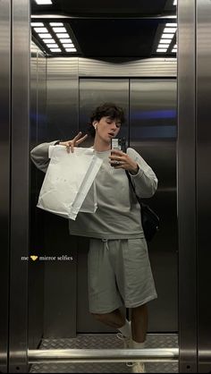 a man standing in front of an elevator holding a cell phone and looking at his paper bag