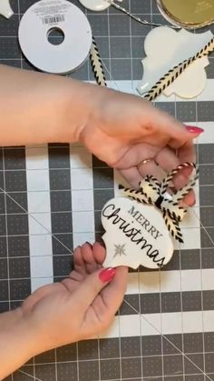 two hands holding a merry christmas ornament on top of a table with other decorations