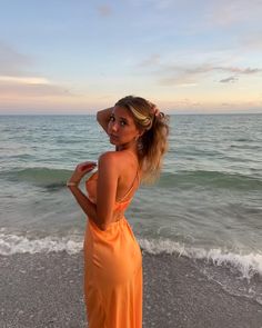 a woman in an orange dress standing on the beach