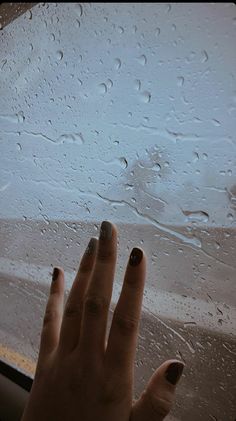 a woman's hand with nail polish on it and raindrops in the background