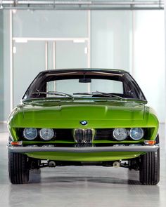 a green car parked in a garage next to a white wall and ceiling with lights