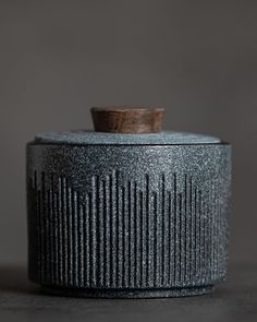 a black container with a wooden top on a gray tableclothed surface in front of a grey wall