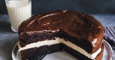 a chocolate cake on a plate with a slice missing from it and a glass of milk in the background