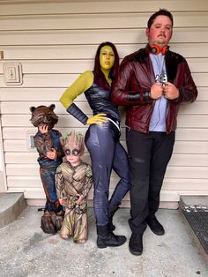 three people dressed up in costumes standing next to each other on the side of a house