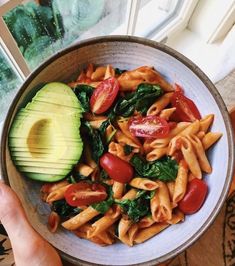 a bowl filled with pasta, tomatoes and spinach next to an avocado