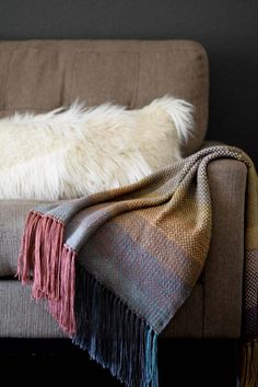 a white dog laying on top of a brown couch next to a blanket and pillow