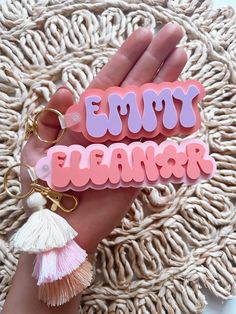 two pink and purple enamel name charms with tassels on top of each one