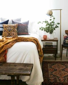 a bed with pillows and blankets on top of it next to a wooden bench in front of a window