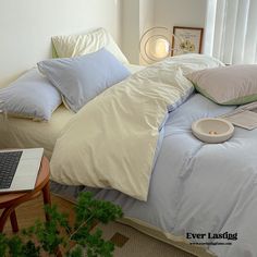 a laptop computer sitting on top of a bed covered in blue and white sheets with pillows