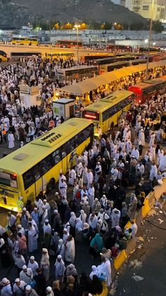 a large group of people standing in front of yellow buses at an outdoor bus station