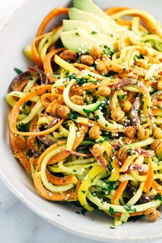 a white bowl filled with zucchini noodles and nuts on top of a table