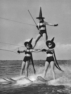 three women in bikinis on water skis wearing witch hats and holding hands with each other